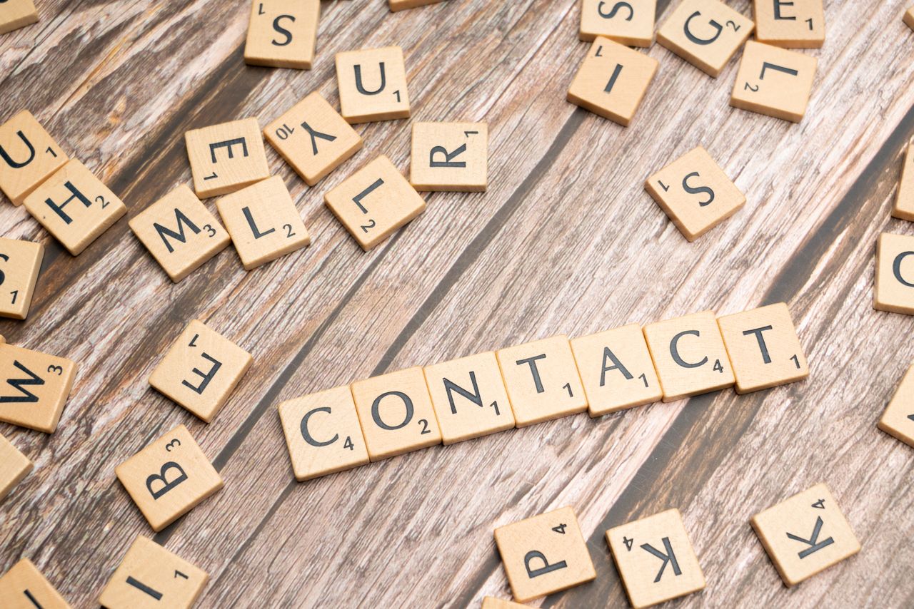 Letter tiles arranged like Scrabble to spell contact on a wooden surface.